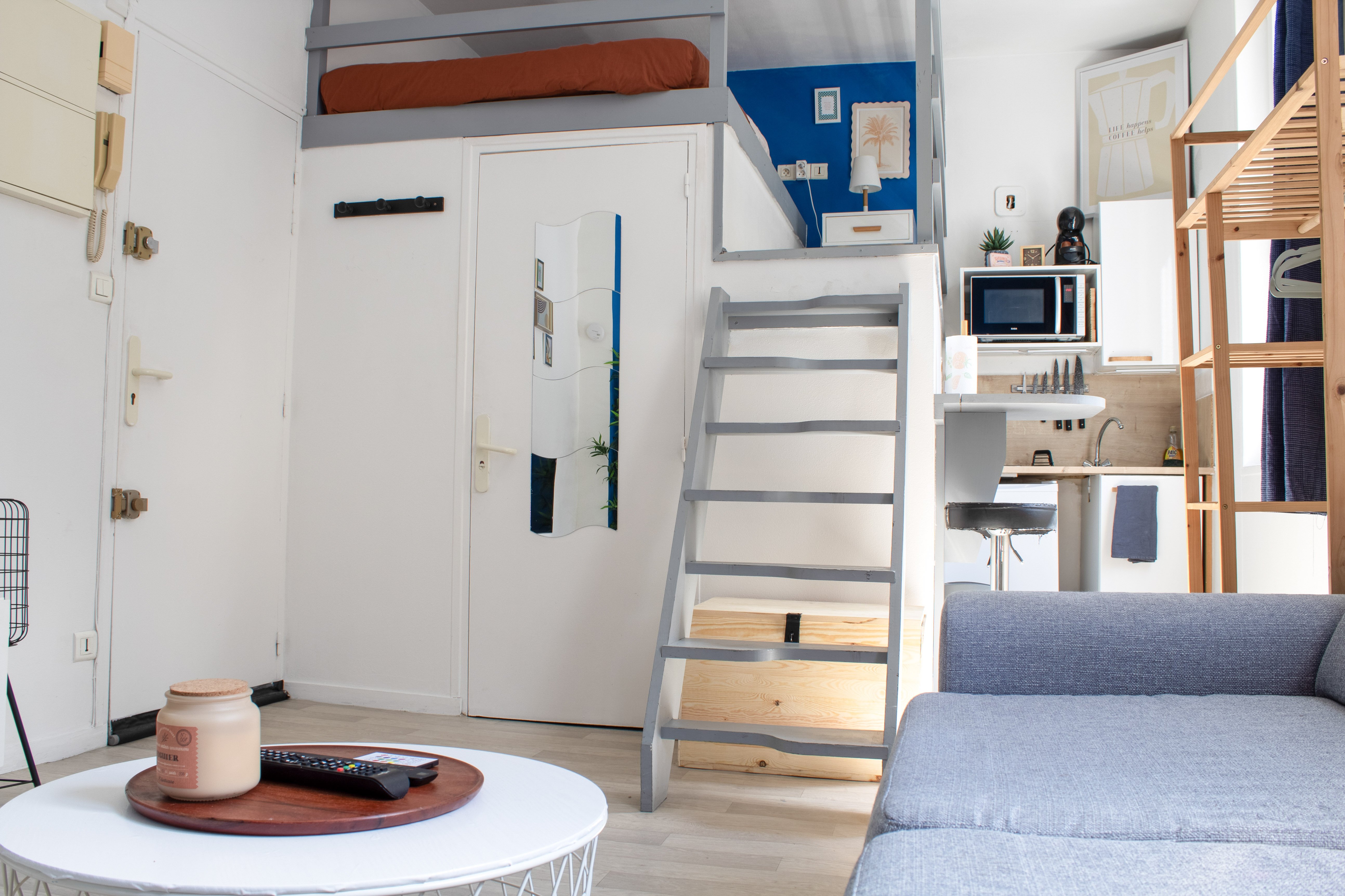 Porte d'entrée du studio, escalier de mezzanine gris et coin cuisine avec micro-ondes