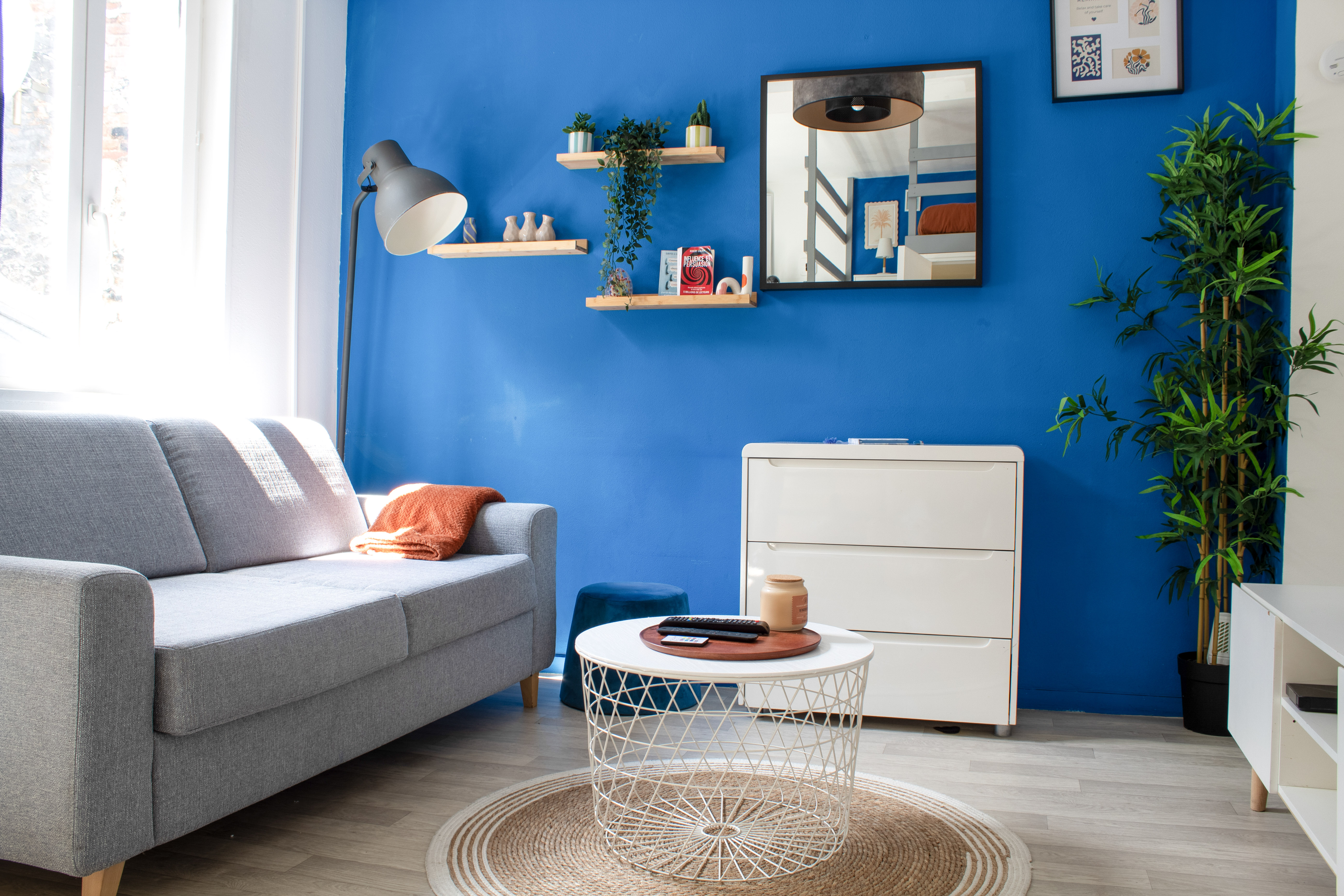 Salon avec canapé gris, table basse, commode blanche et mur bleu avec étagères