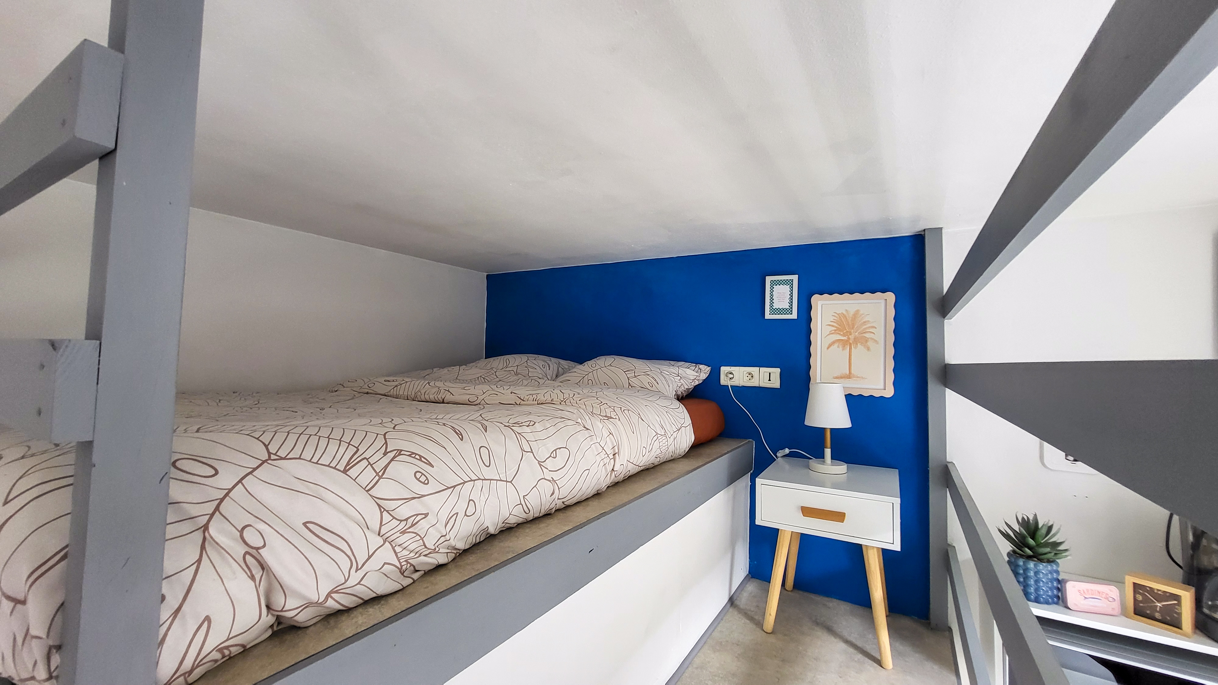 Couchage en mezzanine avec lit double, paroi bleue et table de chevet blanche