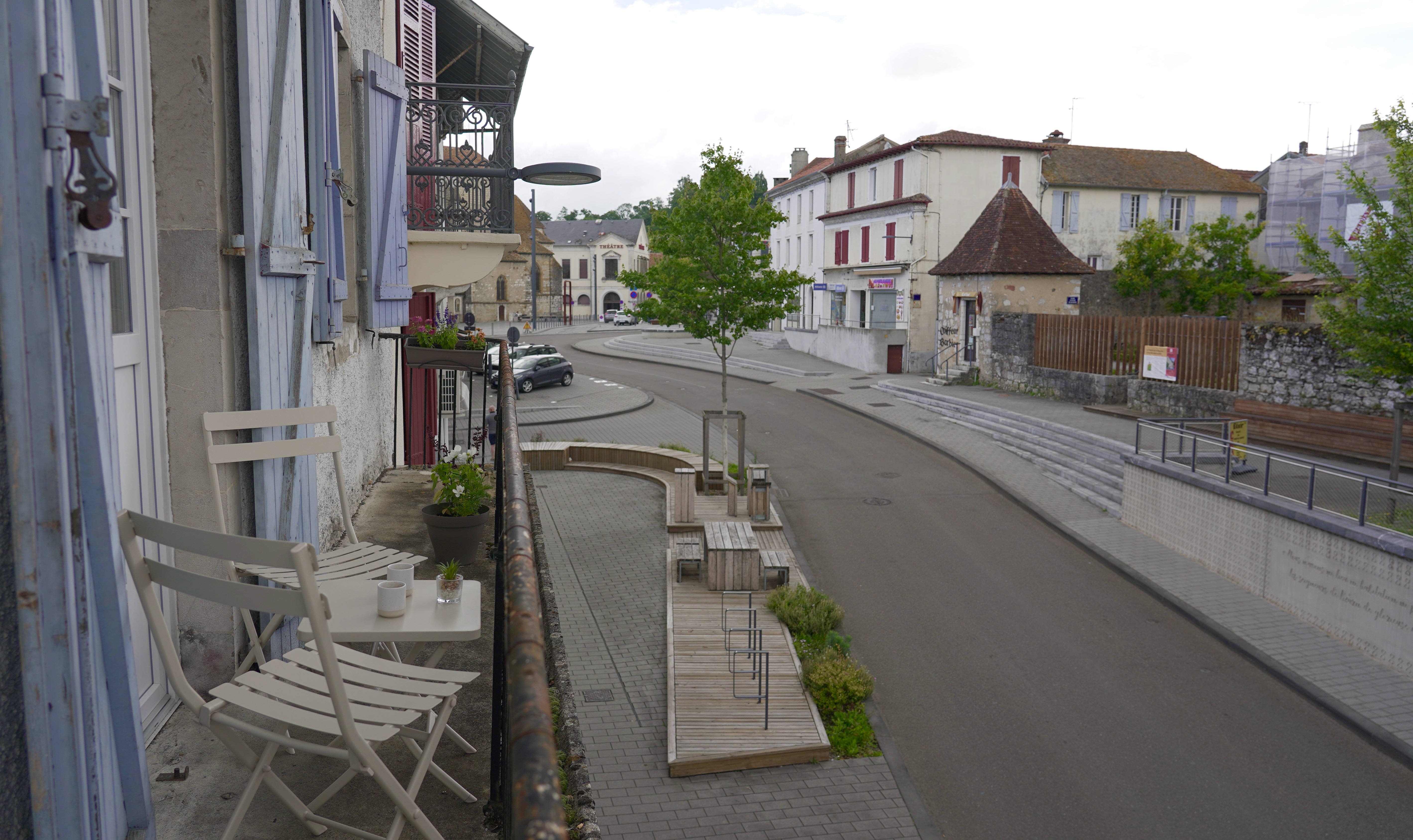 Terrasse avec table et deux chaises blanches donnant sur une rue de centre-ville