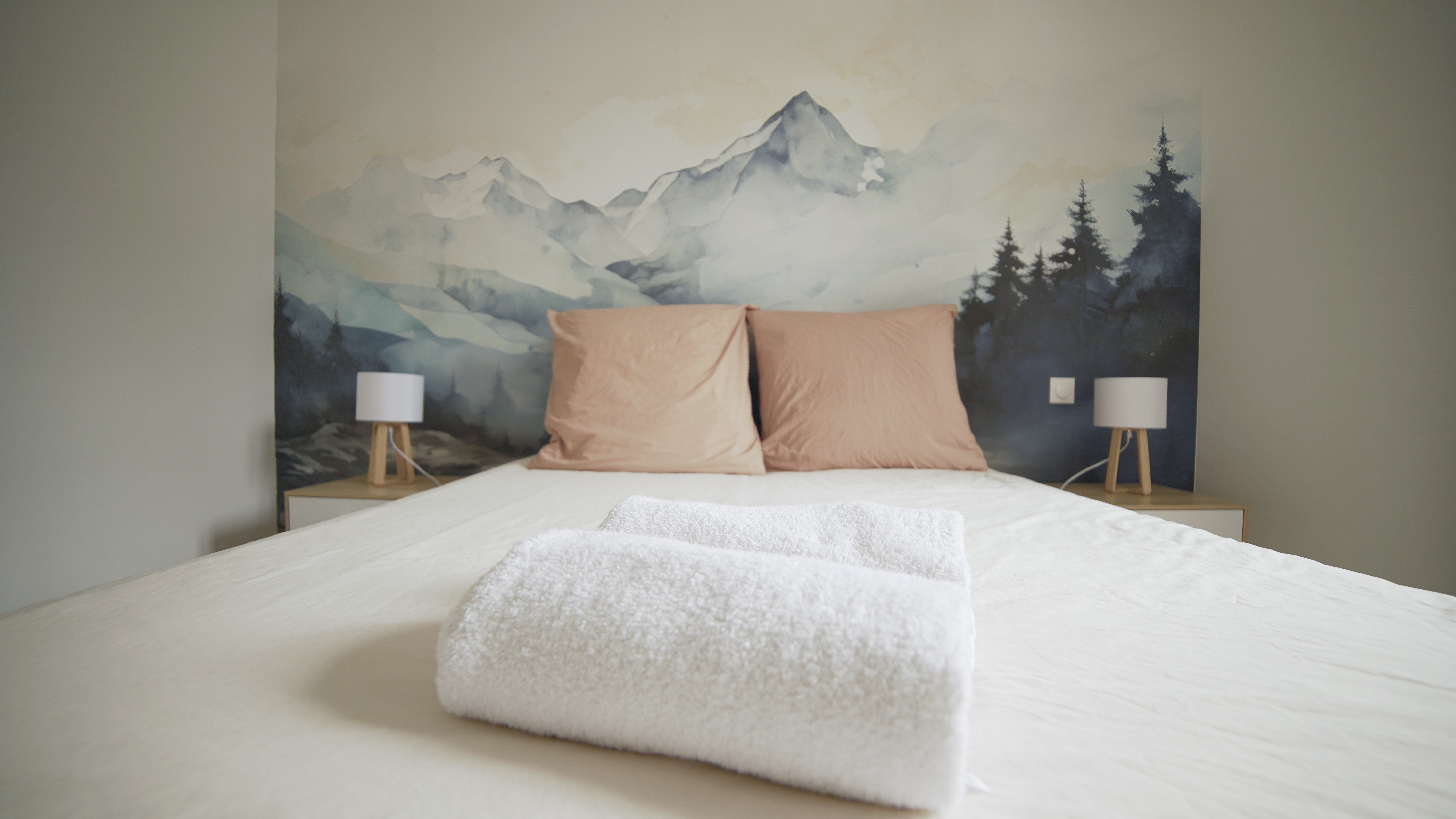 Chambre avec lit double, linge blanc, oreillers roses et fresque murale montagne
