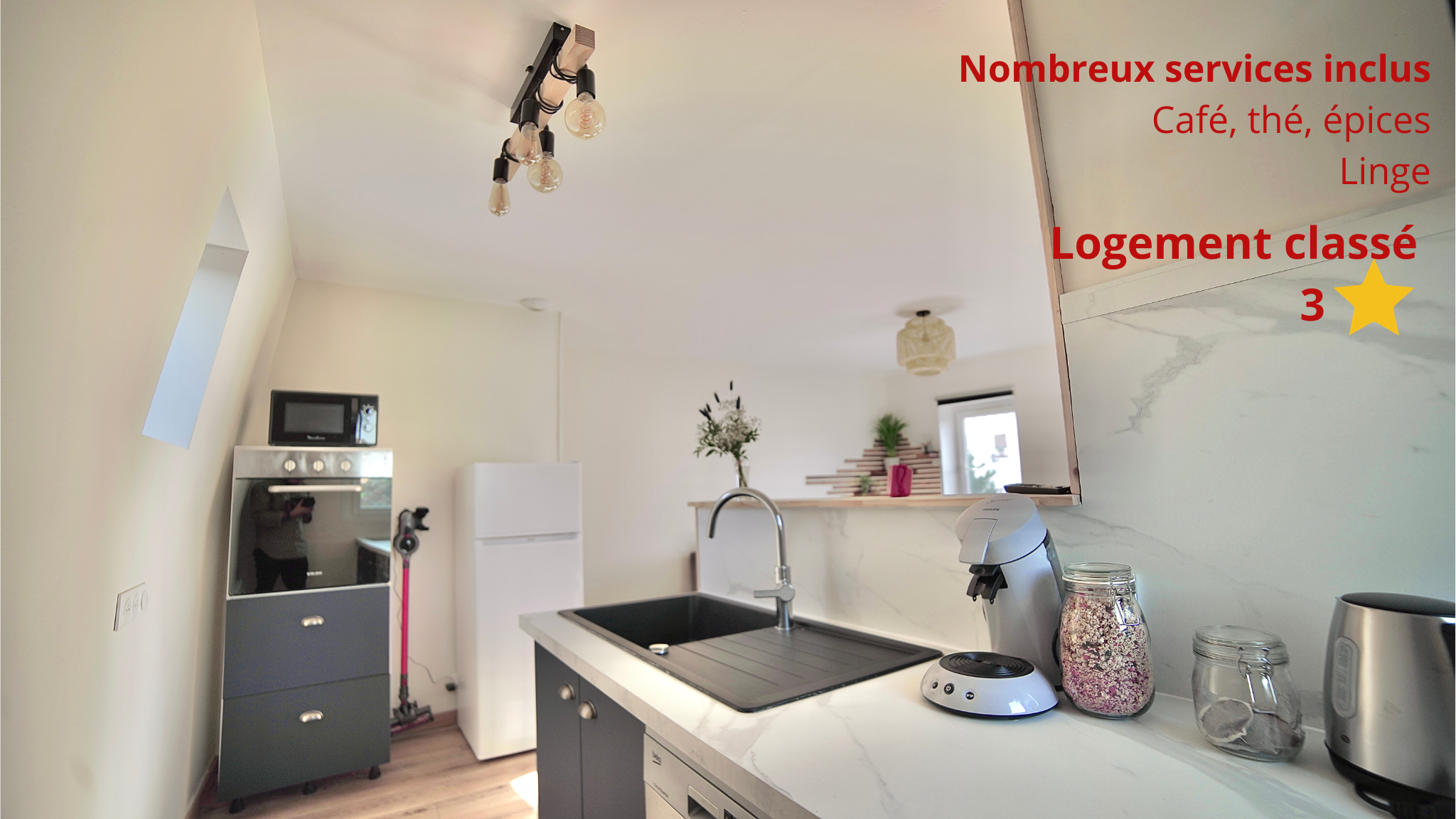 Cuisine équipée avec évier noir, four, micro-ondes, réfrigérateur et machine à café.