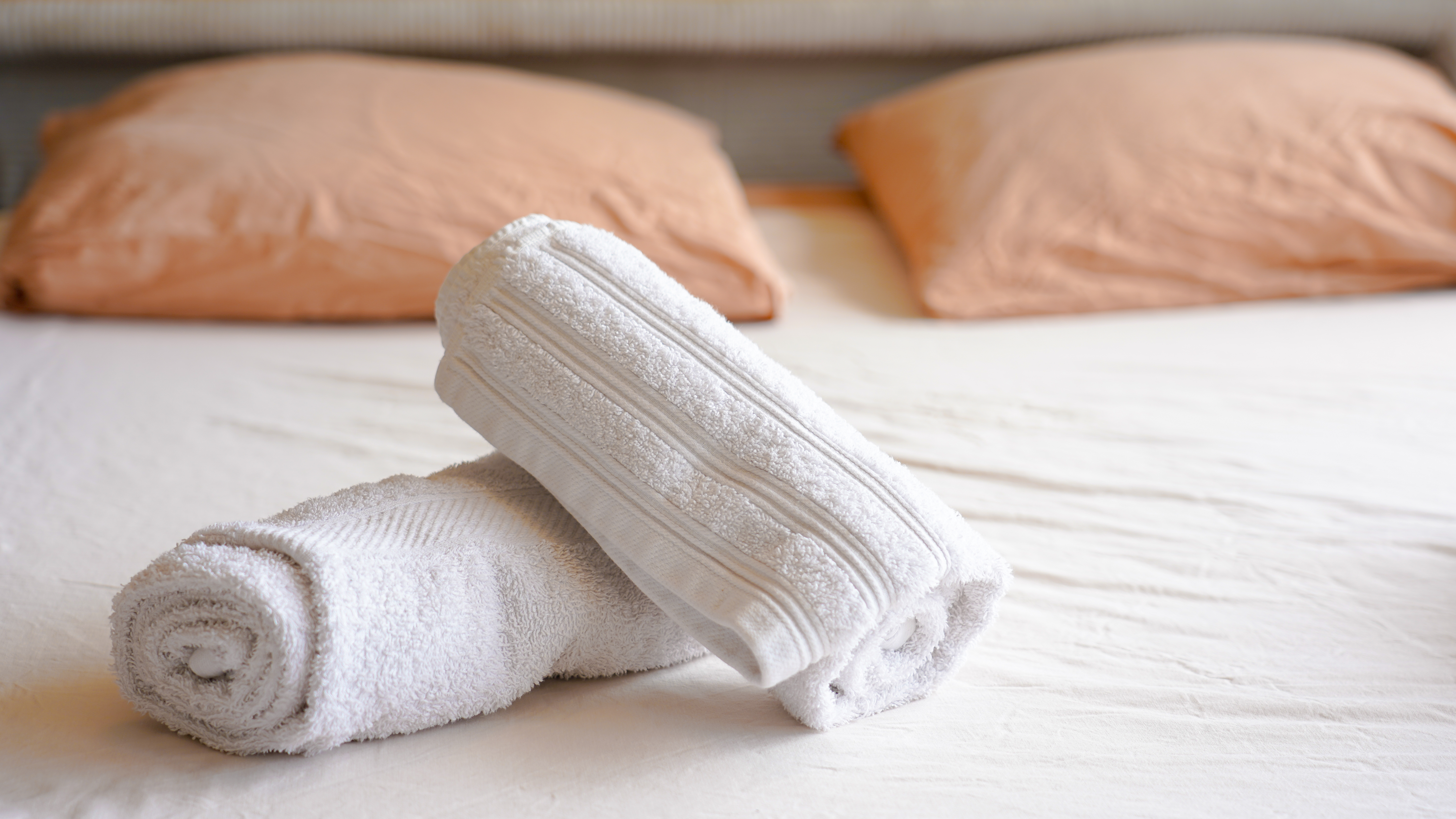 Gros plan sur deux serviettes de bain blanches pliées et roulées, posées sur un lit en draps blancs.