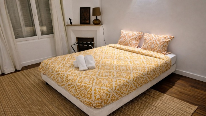 Chambre avec lit double, couette motif doré, serviettes pliées et cheminée décorative.