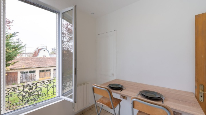 Coin repas avec table en bois et deux chaises, grande fenêtre donnant sur l'extérieur.