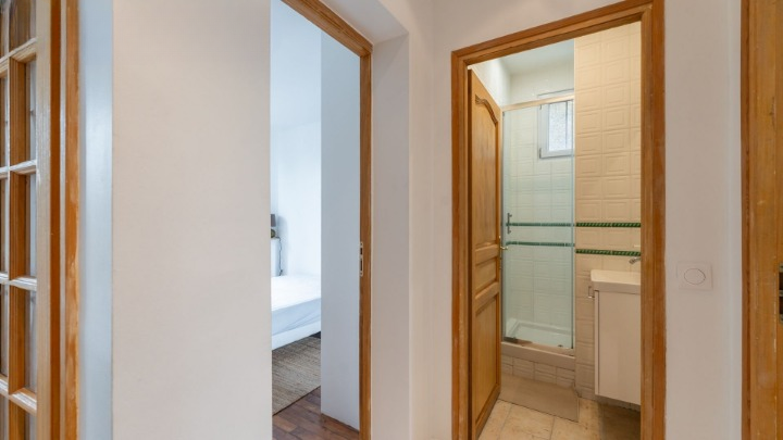 Couloir distribuant une chambre et une salle de douche avec cabine vitrée et lavabo.