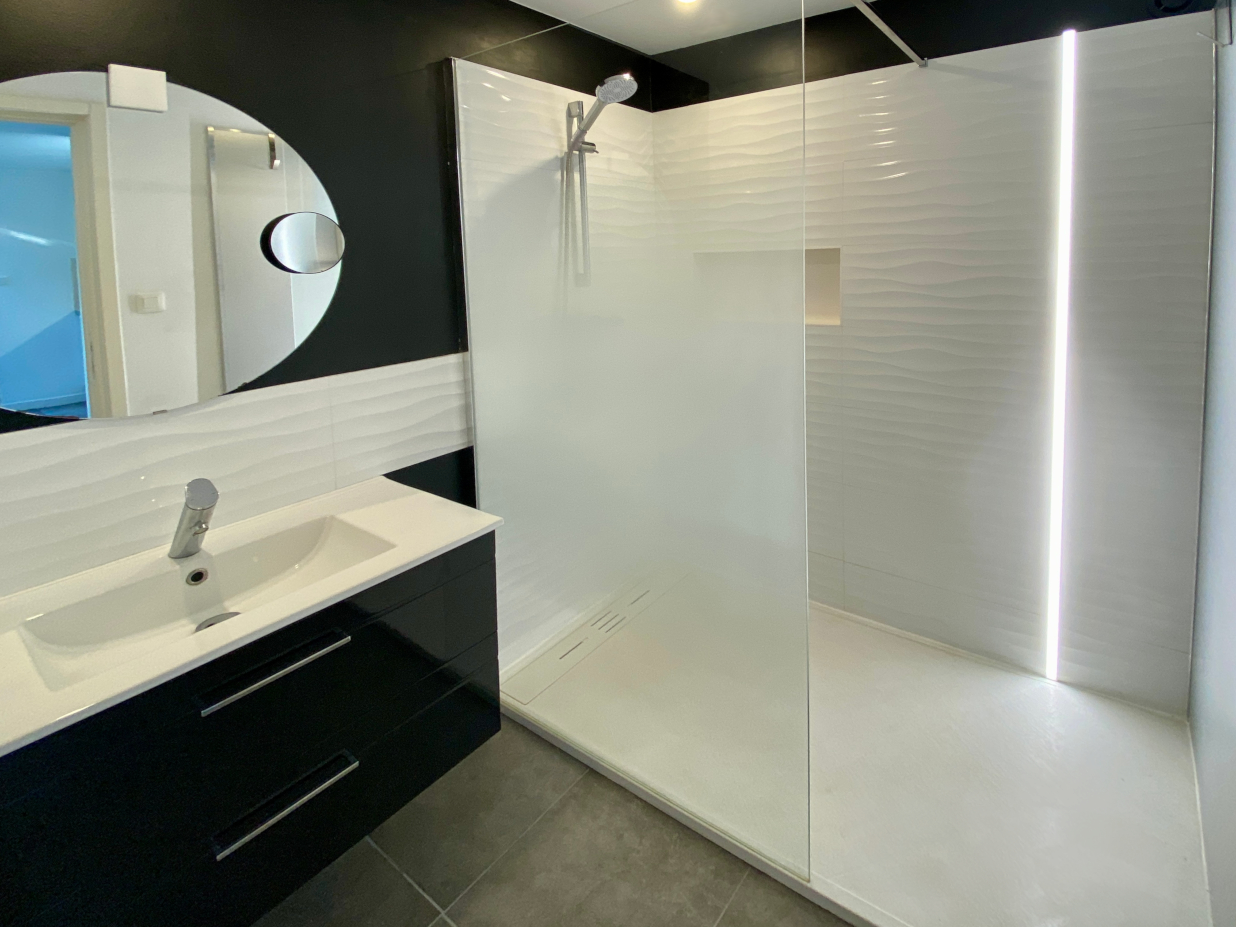 Salle de bain avec douche à l'italienne, paroi en verre, vasque et miroir rond.