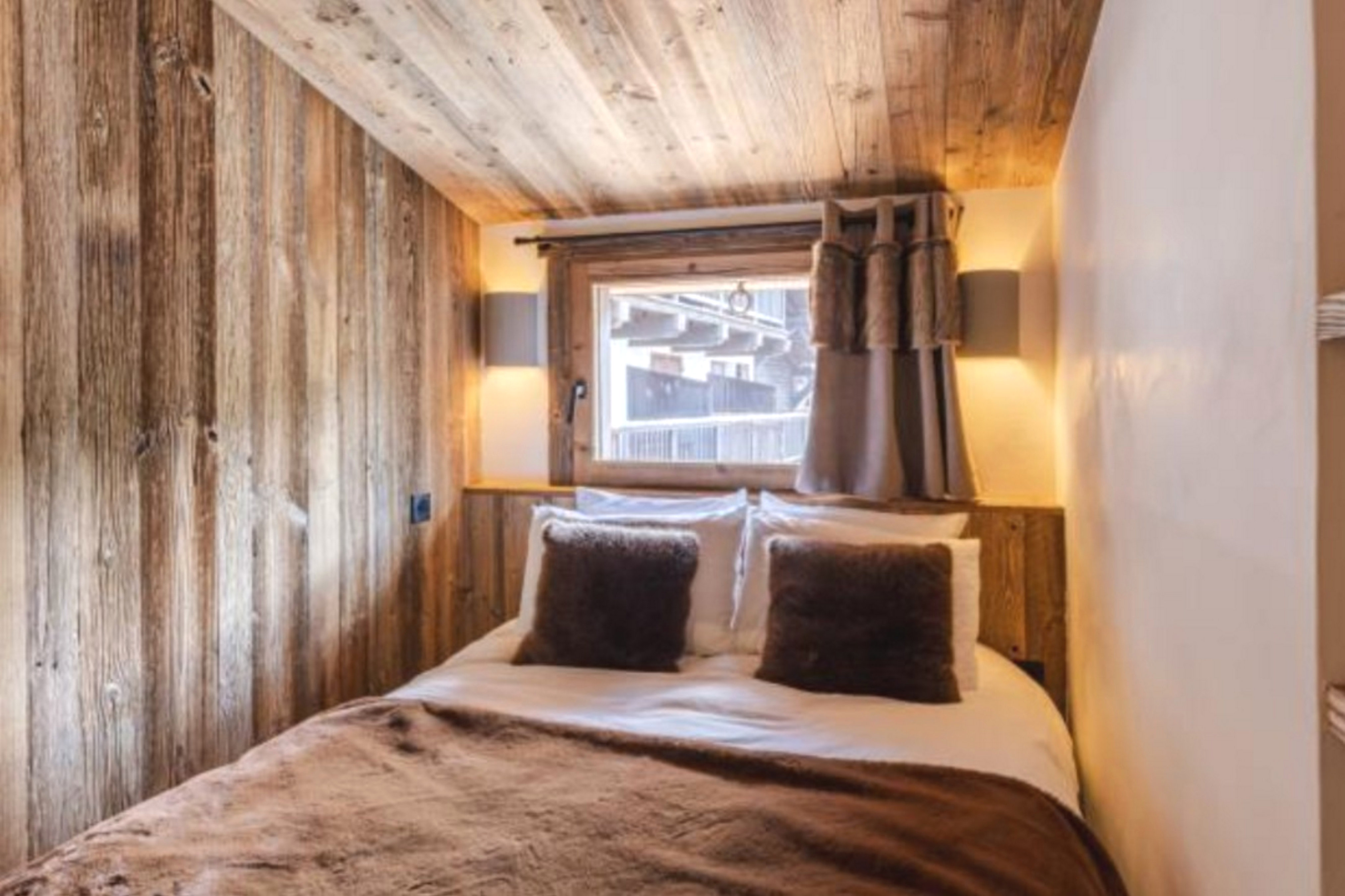 Chambre double avec revêtement bois, lit double, linge blanc et appliques murales.