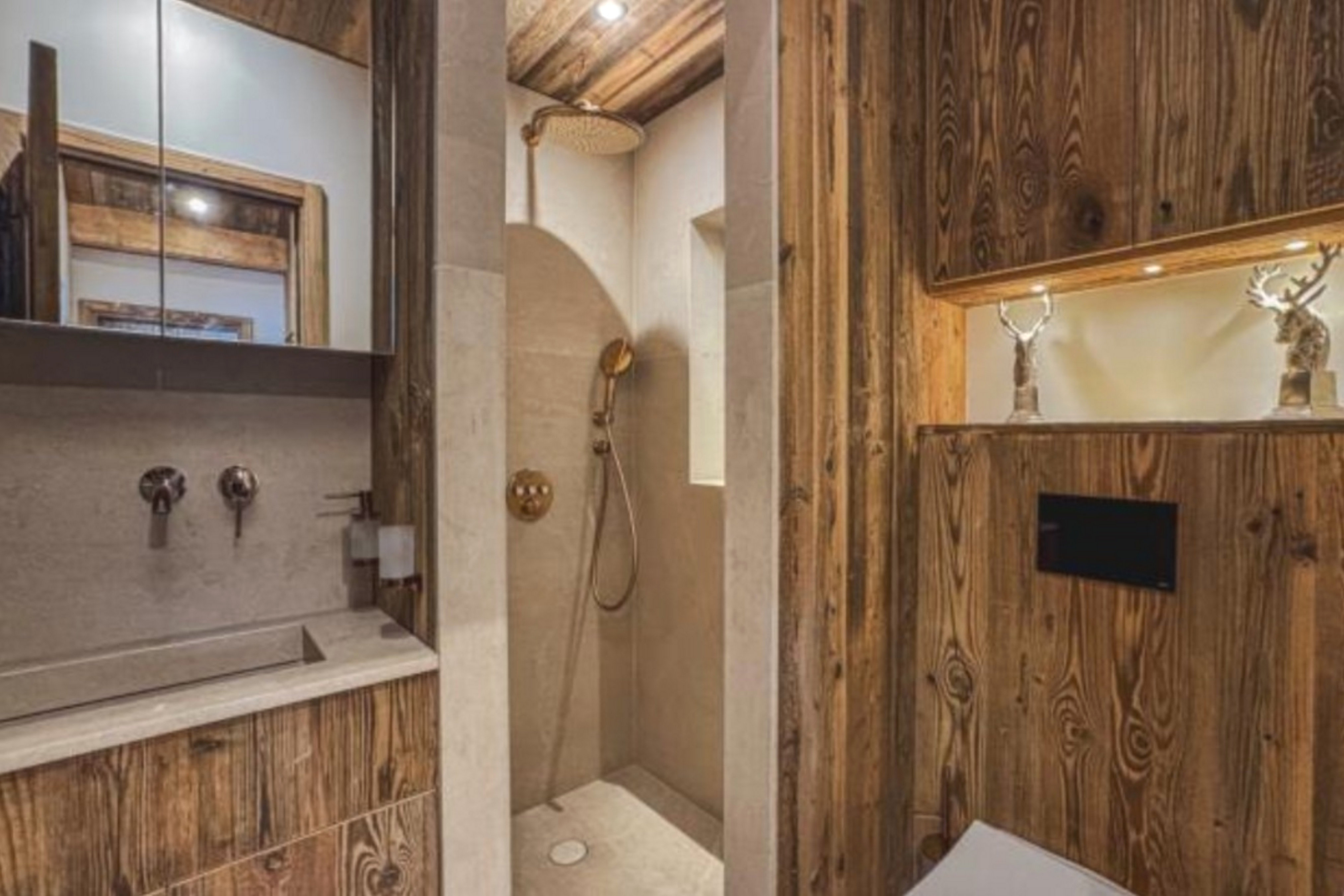 Salle de bain avec douche à effet pluie dorée, vasque et boiseries foncées.